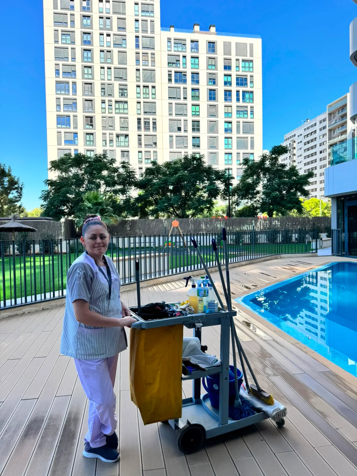 Trabajadora de limpieza con el carrito junto a la piscina de la comunidad
